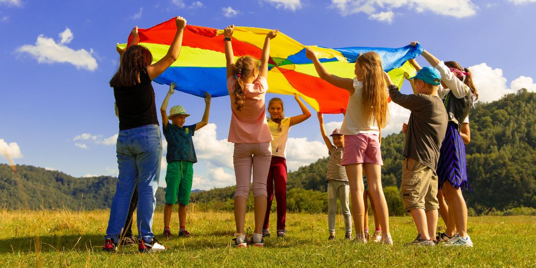 Nine children lifting a parachute in the air whilst stood in a field