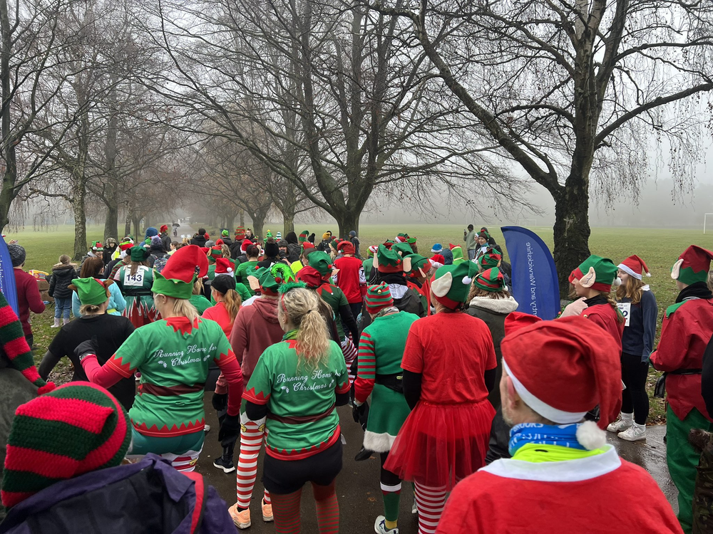 A large group of people dressed as elves get ready to run around a park on a misty day,