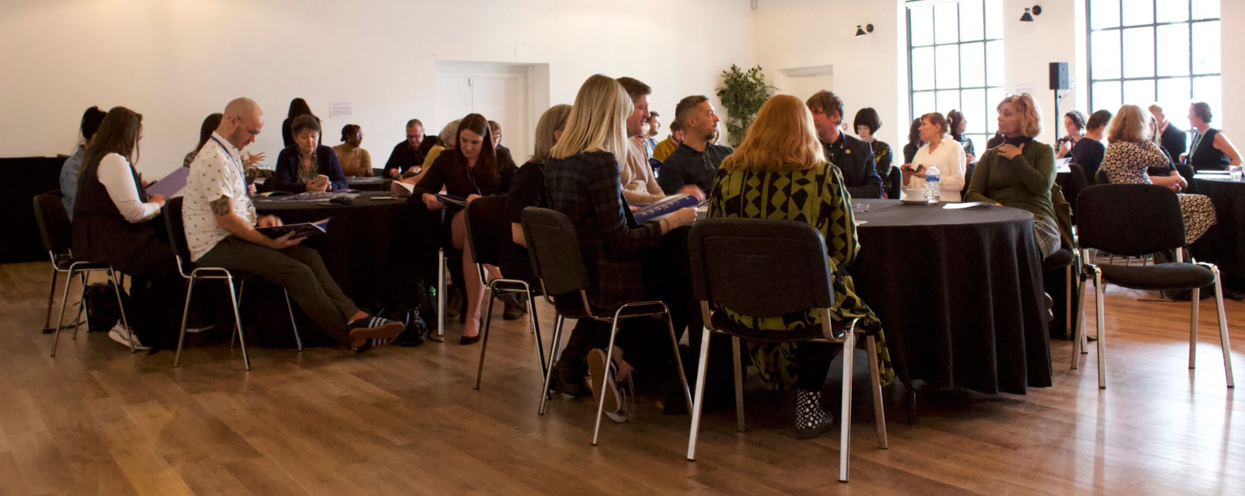 Room of business professionals sat around circle tables with black tablecloths