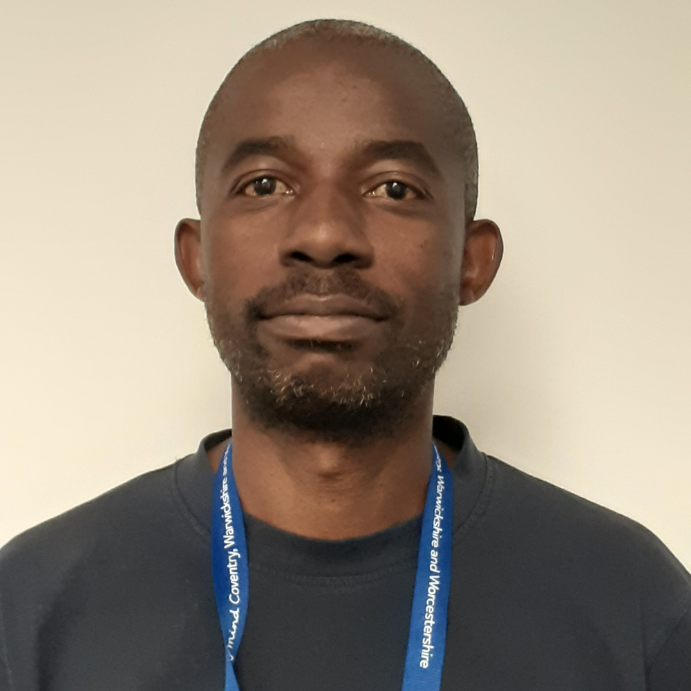 A Black man facing the camera wearing a black shirt and blue lanyard.