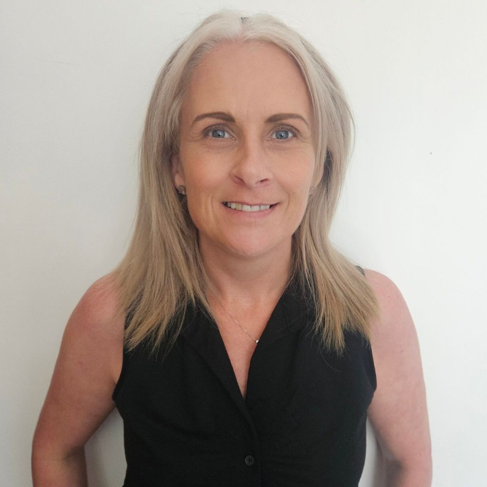 A white lady with should length blonde hair and a black short sleeve top.