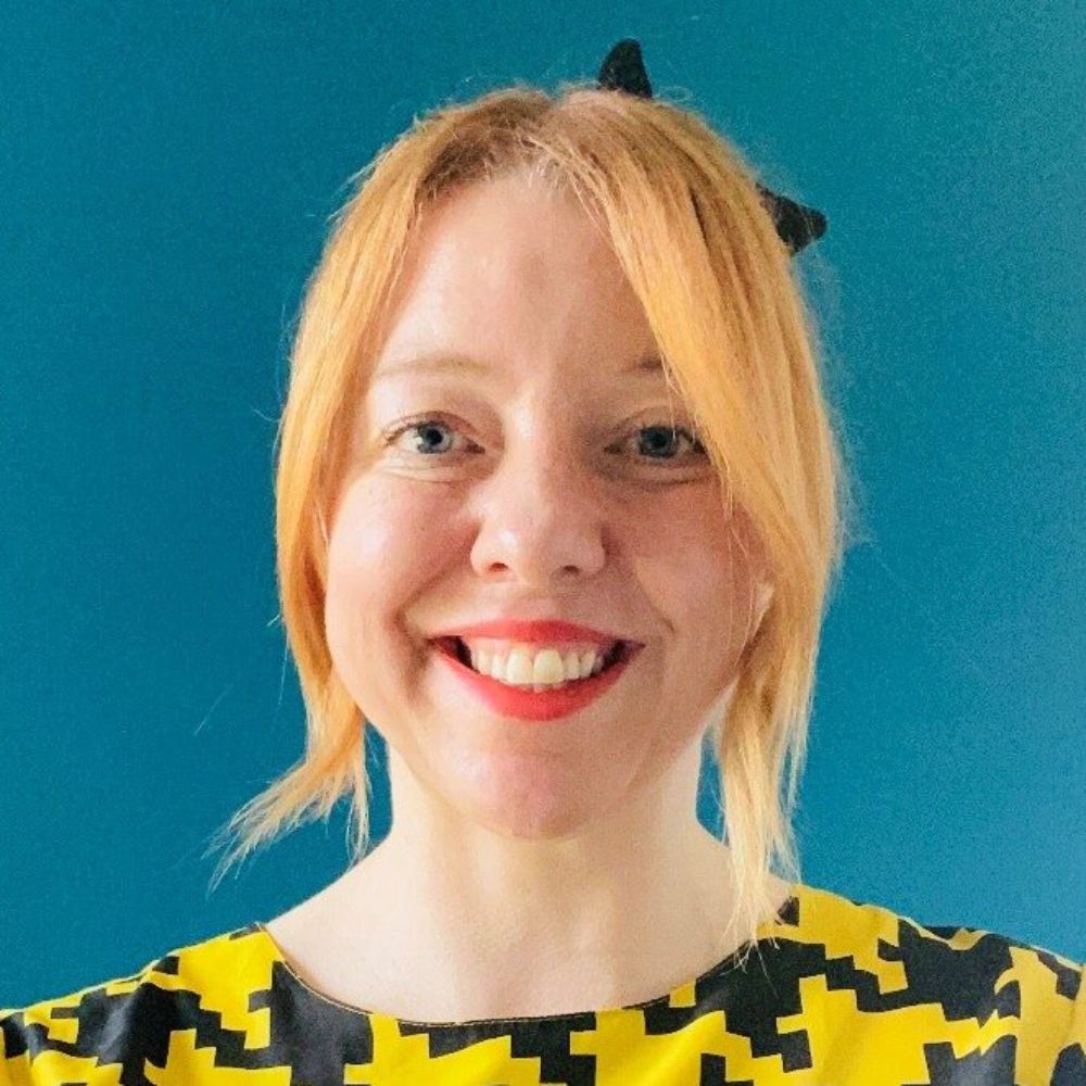 A white lady with ginger head, red lipstick and a yellow and black geometric blouse.