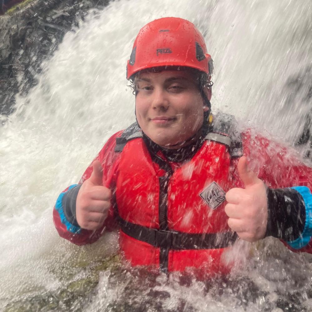 Young man wearing a red helmet and life jacket in rapid waters.