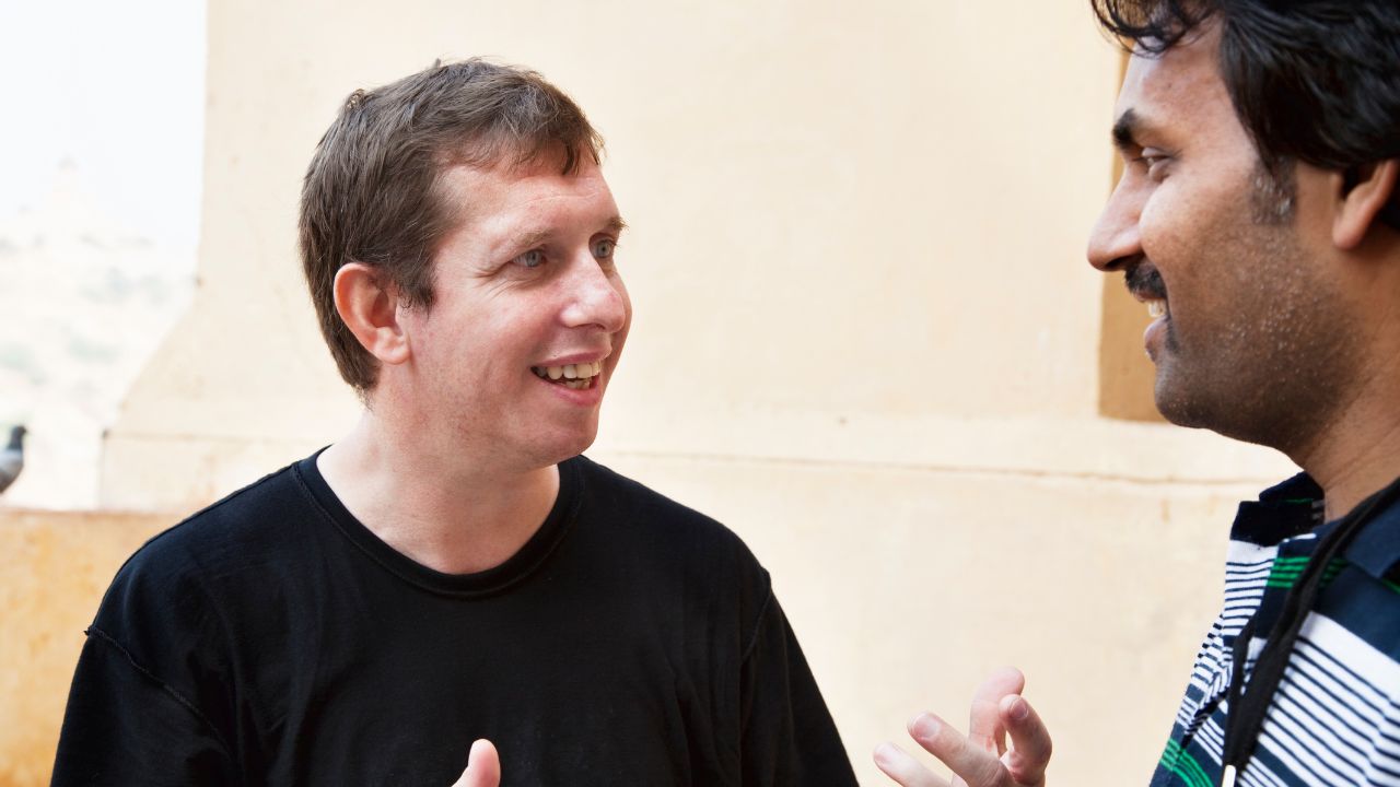 Two men engaged in conversation in a sunny courtyard.